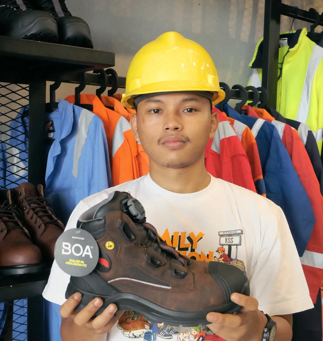 Staf toko memperlihatkan sepatu safety dengan sistem BOA di depan rak pakaian dan sepatu kerja